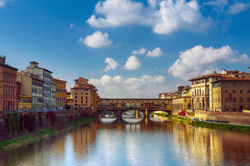 Fototapeta na wymiar View from the river to the famous italian medieval bridge - Ponte Vecchio in Florence with blue sky and clouds, travel outdoor Italy sightseeing background