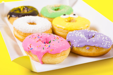 Strawberry, chocklate and other donuts in paper box on yellow background