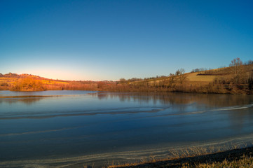 expanse of green grass on the lake with blue sky, countryside and farm around the lake, sunlit water