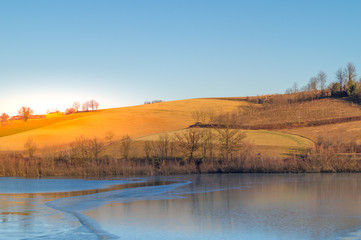 Fototapeta premium expanse of green grass on the lake with blue sky, countryside and farm around the lake, sunlit water