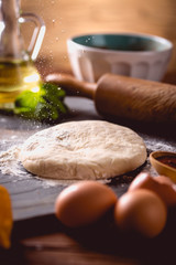 Dough with flour on wooden table, preparing homemade pizza