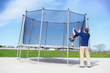 Back view of parent with child and trampoline. Family time on outdoors background