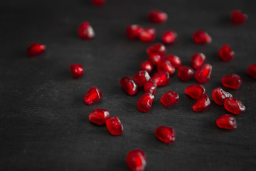 Red juicy ripe pomegranate grains on dark wooden background. View from above. Space for text.