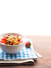 Smoothie bowl with yogurt, strawberries, dried fruit, pistachio nuts, raisins and chia seeds on checkered napkin and wooden table. Vertical. Copy space on white