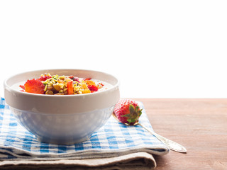Smoothie bowl with yogurt, strawberries, dried fruit, pistachio nuts, raisins and chia seeds on checkered napkin and wooden table