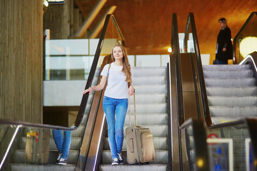 Tourist girl with backpack and carry on luggage in international airport, on escalator