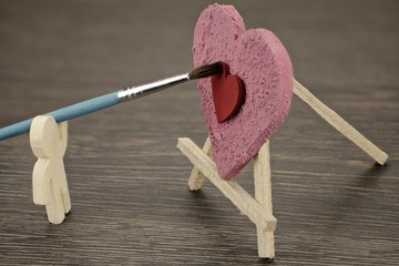 Holzmännchen malt ein Herz mit roter Farbe