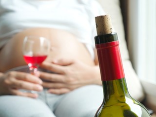 Wine bottle with background of pregnant woman with glass of wine in hand