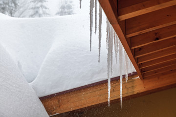Icicle hanging from a wooden roof at winter on snow background