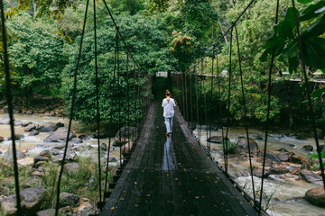 Women goes on the rope bridge across the river in the forest aft