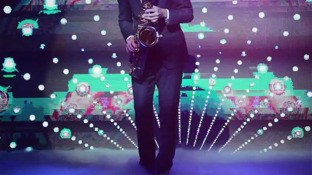 Playing saxophone in night club no face close up hands and legs only. Saxophonist playing his instrument at new years party with strobing and glitching vj screen projection background 