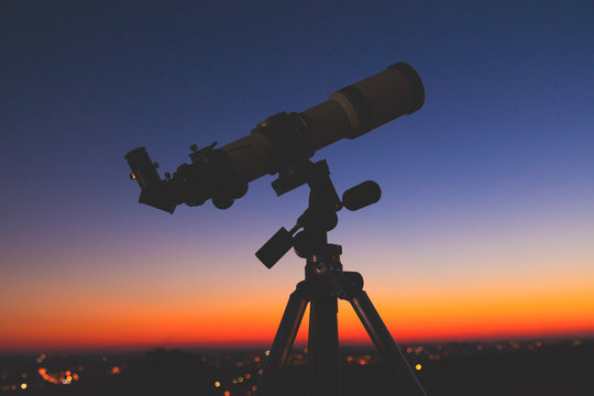 Silhouette of a telescope with de-focused city lights.