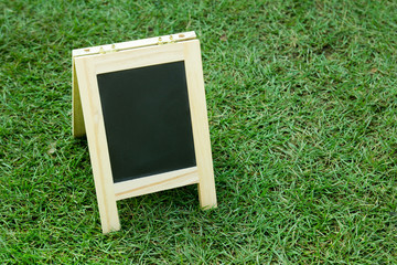 Blank black board with easel on green grass background
