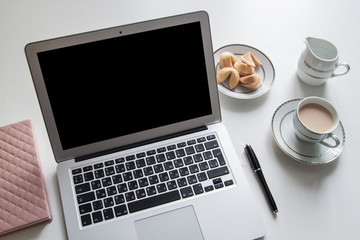 The laptop on a white table with a cup of coffee and biscuits