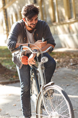 Obraz premium Young handsome guy on a bicycle talking at mobile phone on sidewalk in the city.