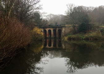 Fototapeta na wymiar Stone bridge reflecting on water in autumn in Hampstead Heath in London, United Kingdom.