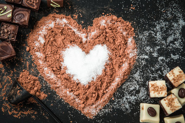 Delicious chocolate candies, truffles with a cocoa heart shape on the black background.