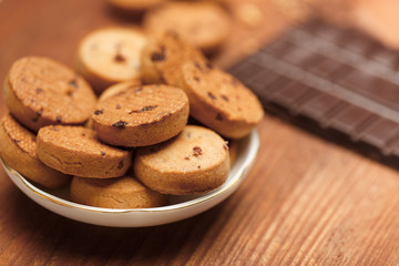 Biscuit cookies with chocolate chips standing in plate on wooden