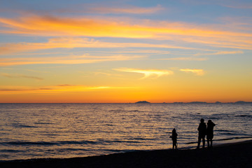 silhouette of family standing on the beach watching the sunset