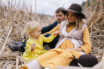 Obraz premium happy young family among dry reeds. pregnant mother, father and little daughter enjoying life outdoor