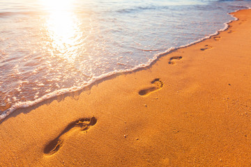 beach, wave and footprints at sunset time