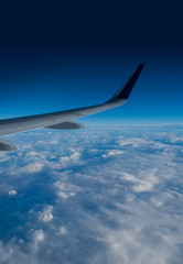 Wing of an airplane flying above the clouds on a clear sunny day