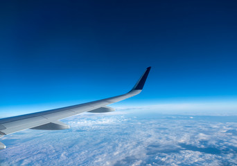Wing of an airplane flying above the clouds on a clear sunny day