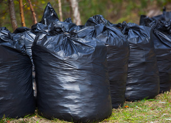Black complete and tied garbage bags standing together on the street outdoors. removal sorting and...
