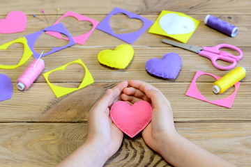 Little girl made a felt heart ornaments. Girl holding a felt heart in his hands. Crafts for Valentine's day or mother's day. Handmade decor. How to create felt valentine ornaments. Easy kids crafts