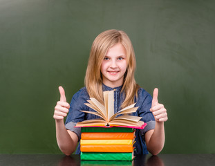 Happy schoolgirl in classroom showing thumbs up