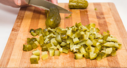 Woman's hands on the wooden board with a knife cutting a pickled cucumber for salad. Healthy eating and lifestyle.