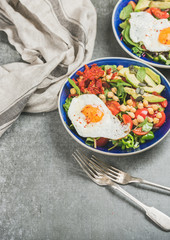 Healthy breakfast with fried egg, chickpea sprouts, seeds, fresh vegetables and greens in bowls over grey concrete background, selective focus, copy space. Healthy lifestyle, dieting food concept