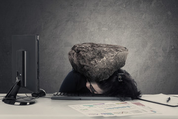 Frustrated woman sleeps on desk with stone