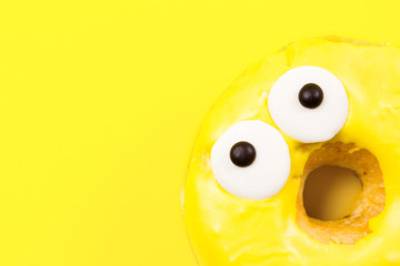 Round donut with eyes on yellow background. Flat lay, top view.