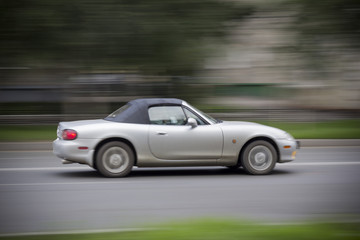 Cabriolet car racing on road. Convertible with a closed top rushing down the road. Everything is blurred.