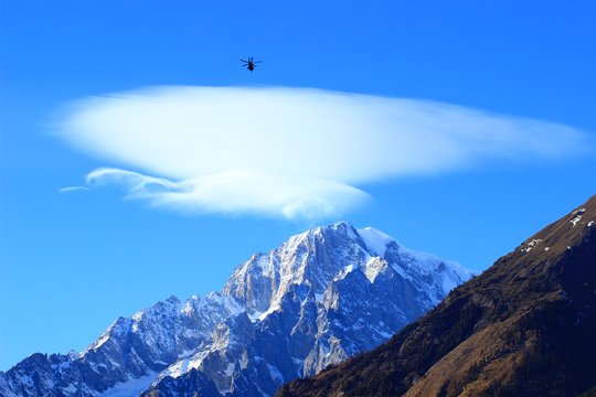 Rescue helicopter in flight, Mont Blanc peak with lenticularis cloud above in background 