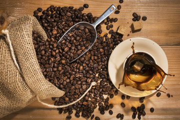 tazzina di caffè con schizzo e sacco di iuta con chicchi di caffè su fondo legno