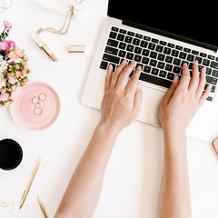 Top view office desk. Workspace with girl's hands, laptop, wildflowers bouquet, coffee cup, golden pen and clips, clipboard. Flat lay