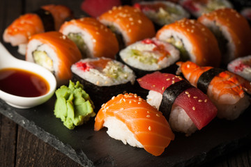 Sashimi and sushi rolls on a stone slatter. Sushi set with salmon, prawns, soy souce, wasabi and ginger. Traditional Japanese cuisine.
