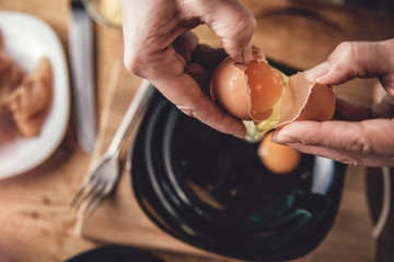 Woman cooking and breaking eggs into the plate