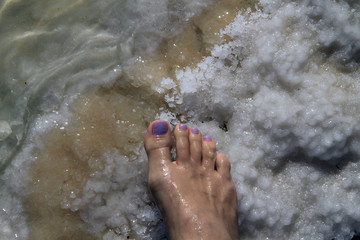 Female foot with pedicure stands on Dead Sea salt