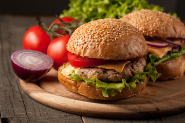 Close-up photo of home made hamburger with beer made of beef, onion, tomato, lettuce, cheese and spices. Fresh burger closeup on wooden rustic table with potato fries and chips.