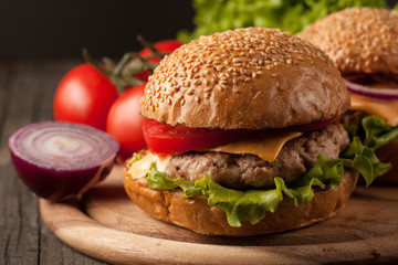 Close-up photo of home made hamburger with beer made of beef, onion, tomato, lettuce, cheese and spices. Fresh burger closeup on wooden rustic table with potato fries and chips.