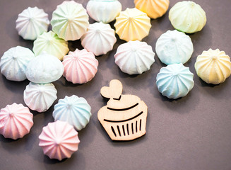 meringues in pastel colors with wooden figure of cupcake on grey background.