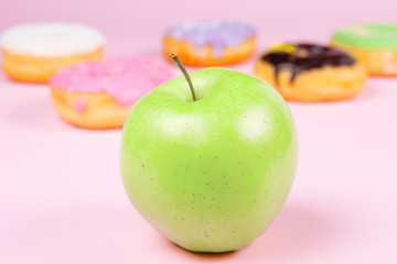 Close-up of tasty donuts and fresh green apple on pink background suggesting healthy food concept