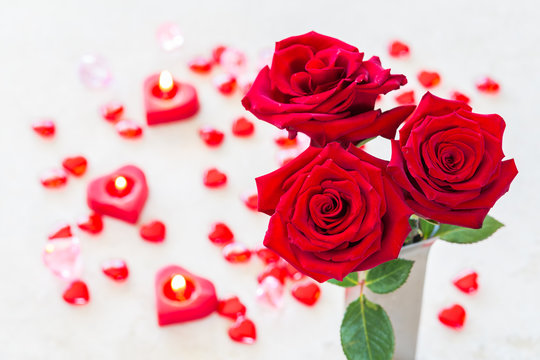 3 roses in the vase/Valentines concept with 3 roses, heart shaped candles and Translucent Red Acrylic Hearts on the rustic table.