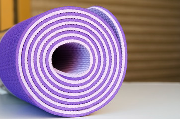 Fototapeta na wymiar Close up of rolled violet yoga mat for practicing yoga,pilates or fitness. Active sport background. Shallow deep of field