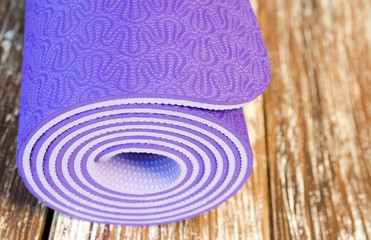 Fototapeta na wymiar Close up of rolled violet yoga mat for practicing yoga,pilates or fitness. Active sport background. Shallow deep of field