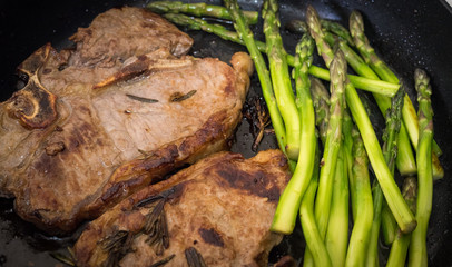 Grilling steak on pan with rosemary and asparagus. Beefsteak cooking on a kitchen. Fresh, delicious, spicy, juicy meat with copy space closeup.