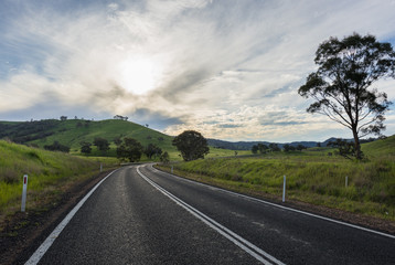 Sunset over rural street with tree and mountain in background.
